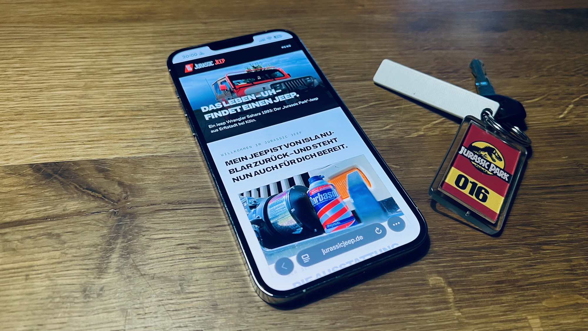 Die Homepage des Jurassic Jeep auf einem Apple iPhone 13 Pro Max, daneben ein Autoschlüssel eines Jeep Wrangler mit „Jurassic Park“-Schlüsselanhänger
